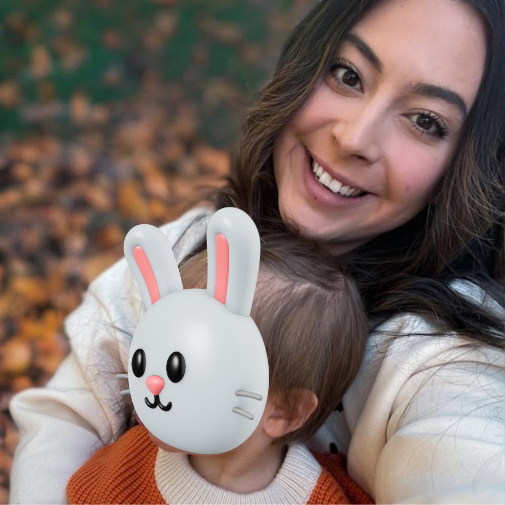 Shairie Espino smiling outdoors in fall, holding her child, whose face is covered with a bunny sticker