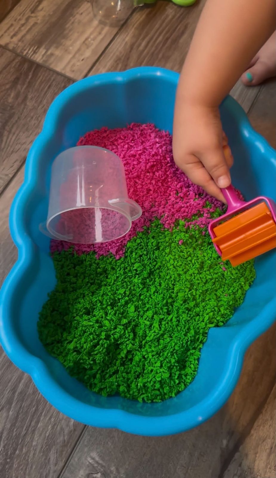 A sensory bin of pink and green rice with scoops